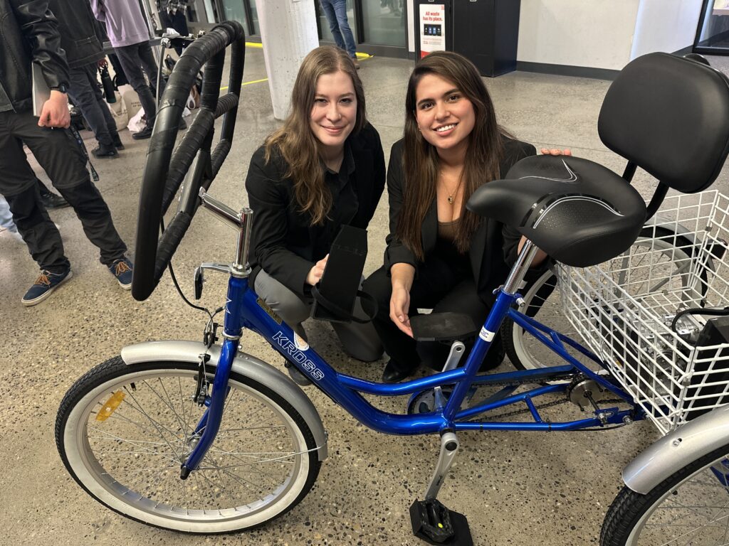 Two female engineers stand with a trike with improved pedals and handlebars