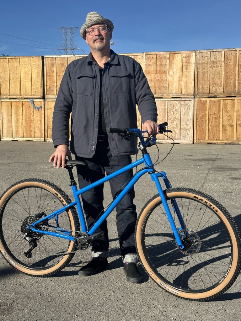 Man in hat stands by a blue custom bike