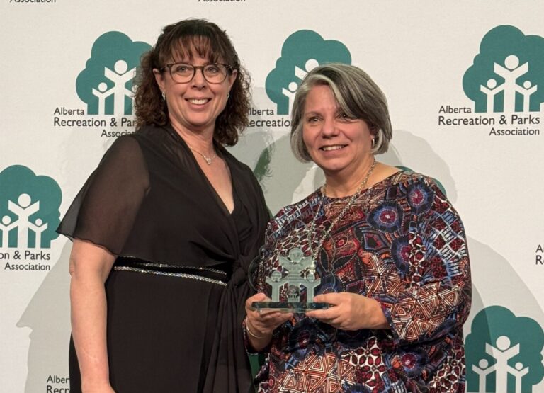 two women stand with a glass award