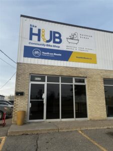 brown brick building with big blue and yellow sign that says bike hub community bike shop, youth en route, and bathtub bikes