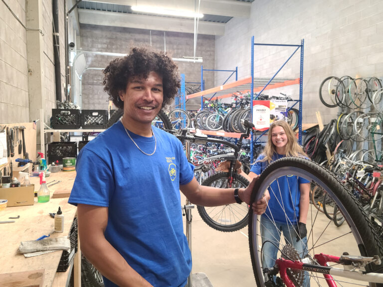 Two of Youth en Route's new summer students, Bon and Mia, standing next to their workstations at the Bike Hub while repairing donated bikes.