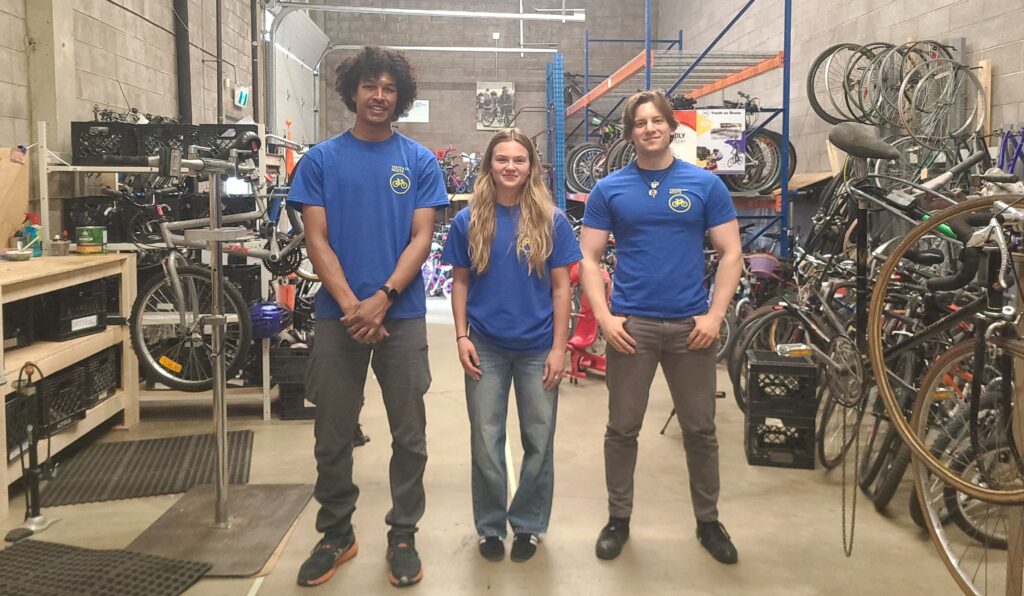 Youth en Route's three new summer students, Bon, Mia and Jakob, standing in the middle of the Bike Hub floor.